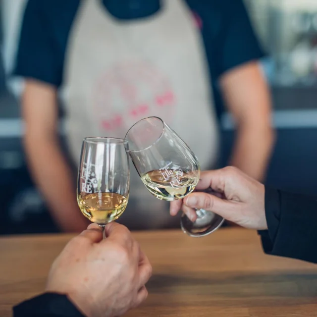 Deux personnes trinquent avec des verres de vin blanc dans une cave.