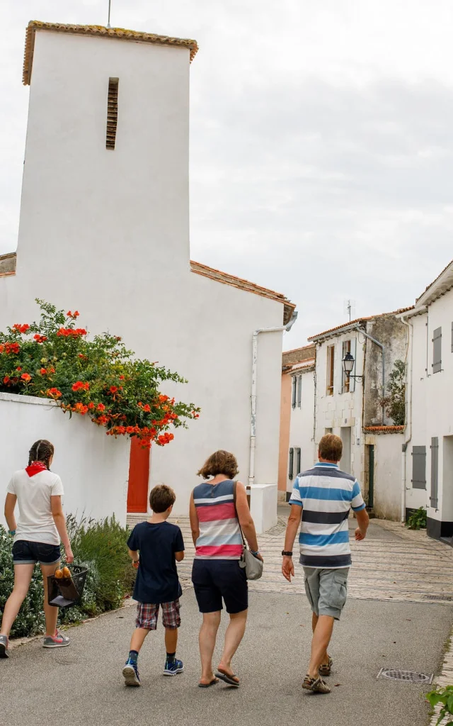 Famille marchant dans une rue avec l’église des Portes-en-Ré.