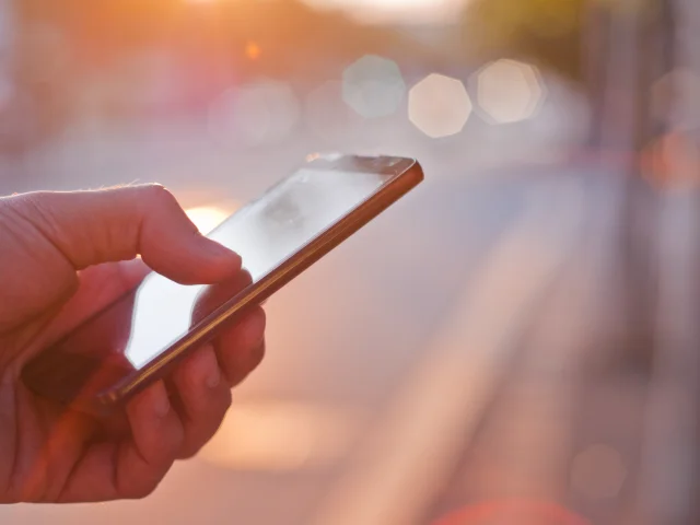 Man using mobile smartphone. Close up of a businessman hand holding and using a smart phone outdoors. Detail of handsome hipster modern businessman using smart phone in the city