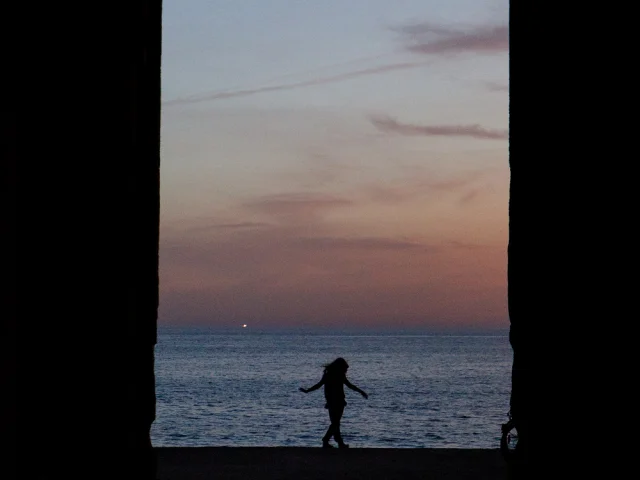 Silhouette d'une personne debout face à l'océan au crépuscule.