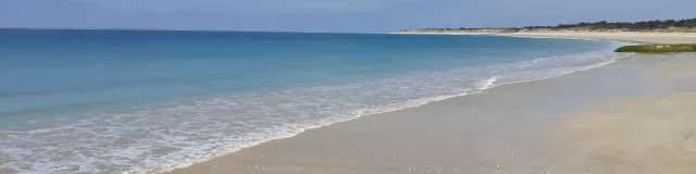 Vue d'une plage de sable fin avec une mer calme et un ciel bleu à Saint-Clément.