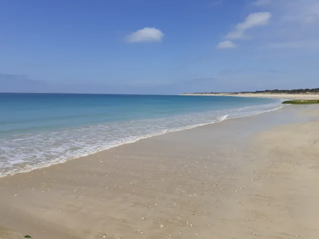 Vue d'une plage de sable fin avec une mer calme et un ciel bleu à Saint-Clément.