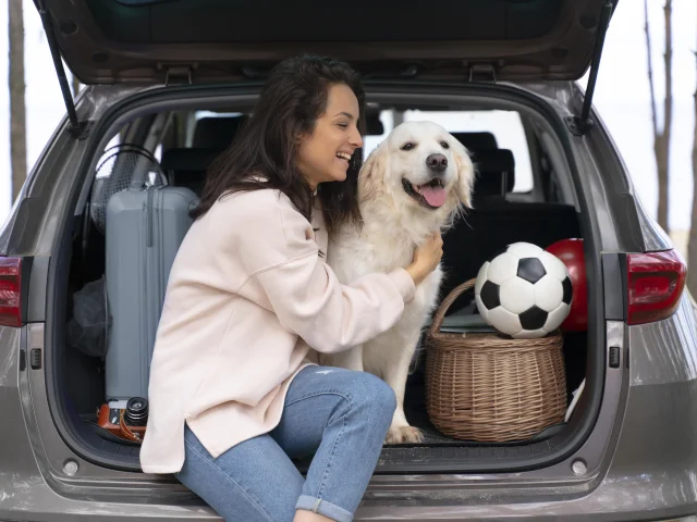 Une femme câline son chien à l'arrière de sa voiture ouverte, avec des bagages.