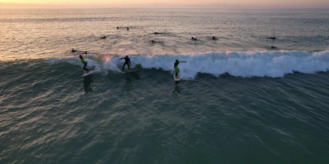 Groupe de surfeurs sur une vague à la plage du Petit Bec