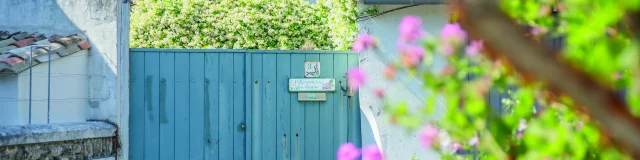 Portail bleu devant une maison avec des fleurs blanches.