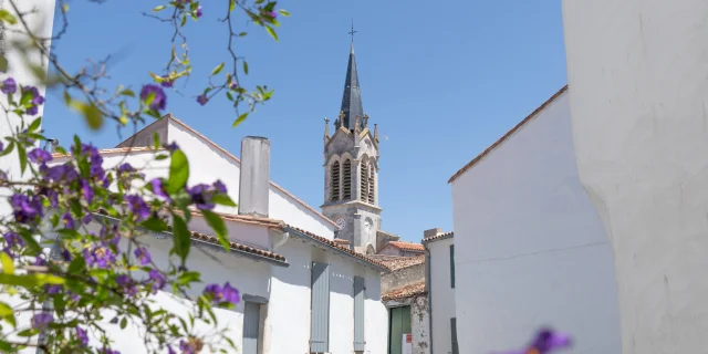 Clocher de l'église vu depuis une rue de La Couarde-sur-Mer avec des fleurs au premier plan.