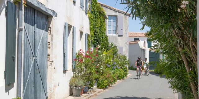 Deux cyclistes se promenant dans une rue fleurie de La Couarde-sur-Mer.