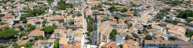 Vue aérienne d'un village avec une église au centre et des toits de tuiles rouges.