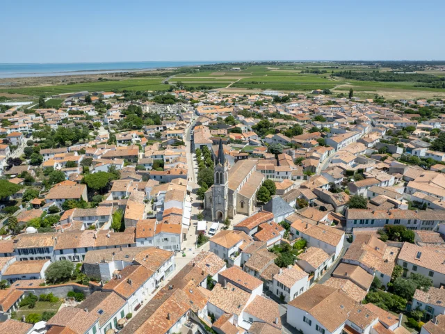 Vue aérienne d'un village avec une église au centre et des toits de tuiles rouges.