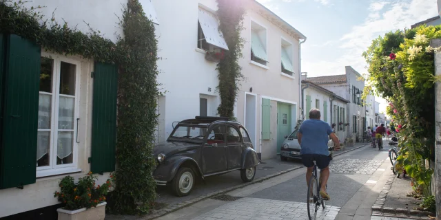 Cycliste dans une rue pittoresque de La Flotte avec une vieille voiture garée.