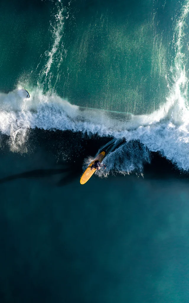 Surfeur capturé en action sur une grande vague vue de haut.