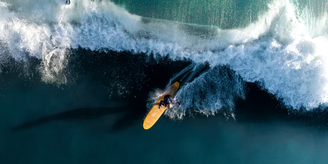 Surfeur capturé en action sur une grande vague vue de haut.