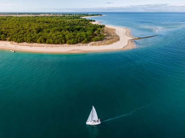 Une vue aérienne de la plage de Trousse-Chemise avec un voilier naviguant.