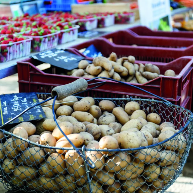 Marché avec des étals de pommes de terre et de fraises.