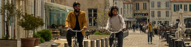 Deux personnes à vélo sur une rue pavée bordée de bâtiments historiques.