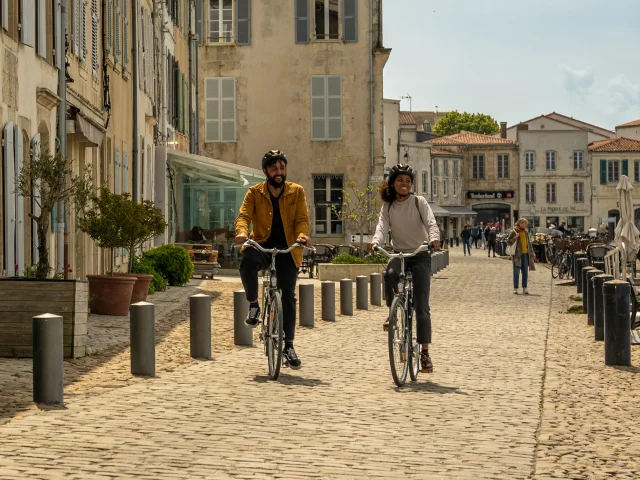 Deux personnes à vélo sur une rue pavée bordée de bâtiments historiques.