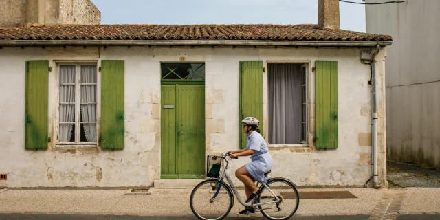 Cycliste passant devant une maison traditionnelle à Sainte-Marie-de-Ré.