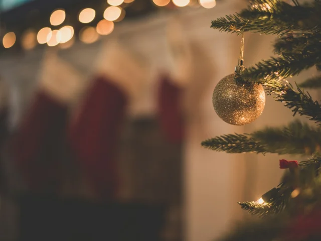 Boule dorée accrochée à un sapin de Noël illuminé avec des guirlandes.