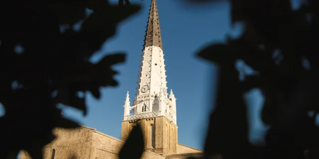 Clocher de l'église d'Ars-en-Ré vu à travers des feuillages.