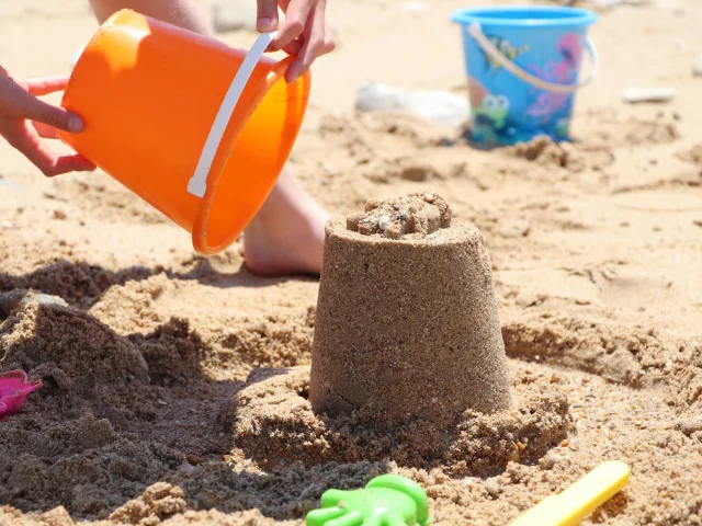 Enfants jouant avec des seaux et du sable sur la plage.