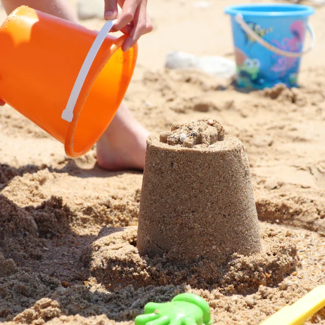 Enfants jouant avec des seaux et du sable sur la plage.