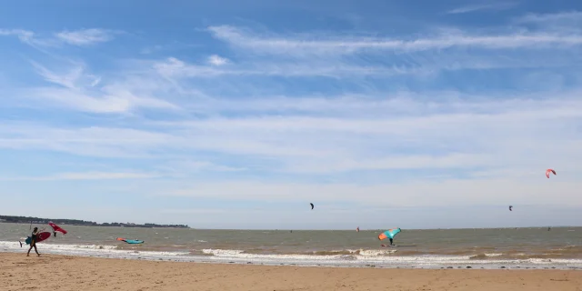 Personne faisant du kitesurf sur une plage sous un ciel bleu dégagé.