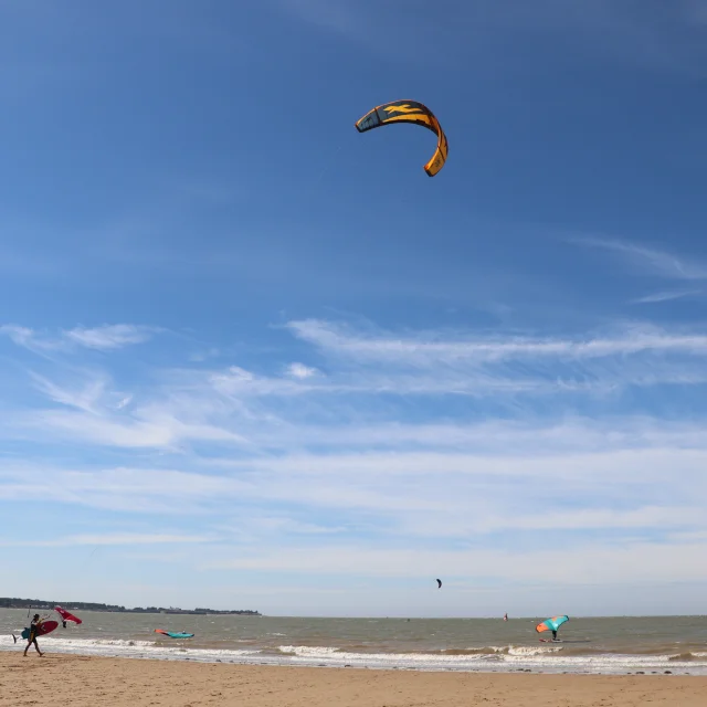 Personne faisant du kitesurf sur une plage sous un ciel bleu dégagé.