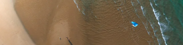 Vue aérienne d'une plage avec un kite surfeur et des vagues.