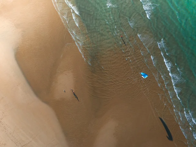 Vue aérienne d'une plage avec un kite surfeur et des vagues.