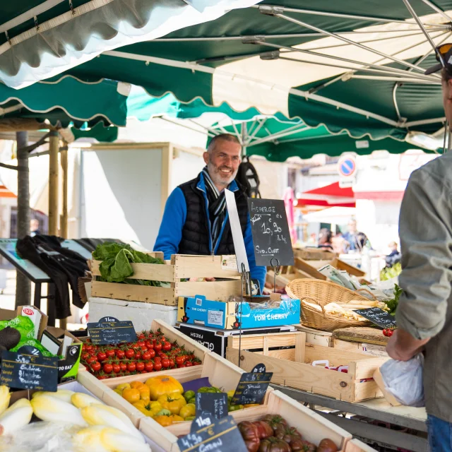 Marché local avec un vendeur souriant et des étals de fruits et légumes.