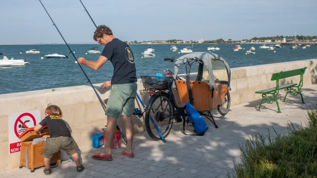 Deux personnes pêchant à la ligne sur le port, entourées de bateaux amarrés.