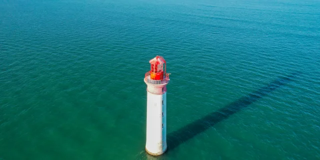 Phare solitaire au milieu de l'océan avec une ombre projetée sur l'eau.