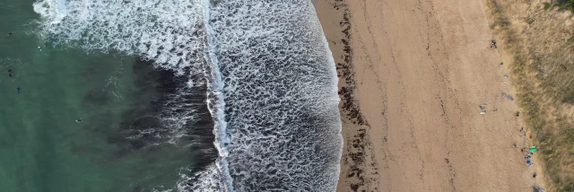 Vue aérienne de la plage du Petit Bec avec des vagues s'écrasant sur le sable.