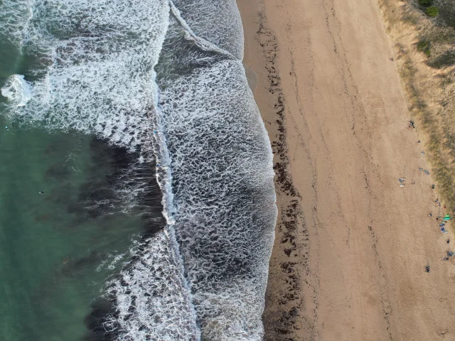 Vue aérienne de la plage du Petit Bec avec des vagues s'écrasant sur le sable.