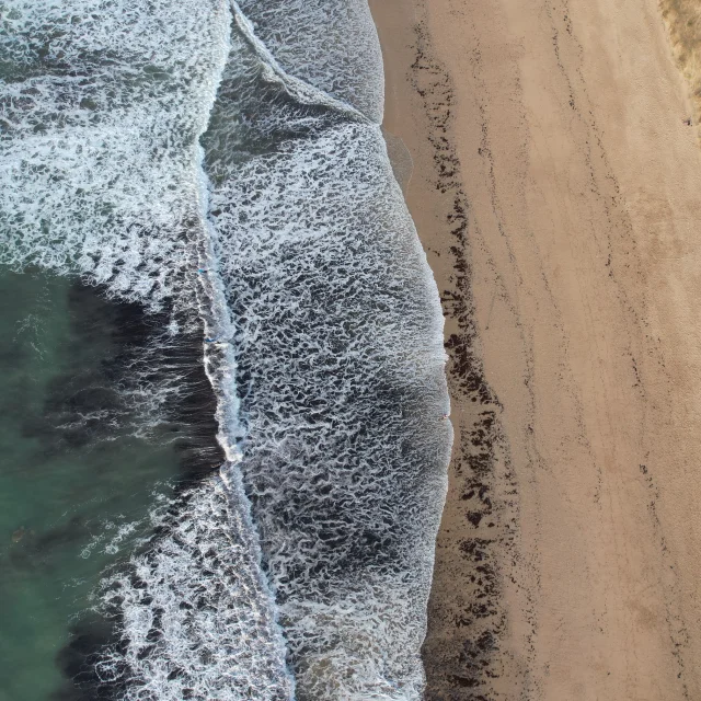 Vue aérienne de la plage du Petit Bec avec des vagues s'écrasant sur le sable.