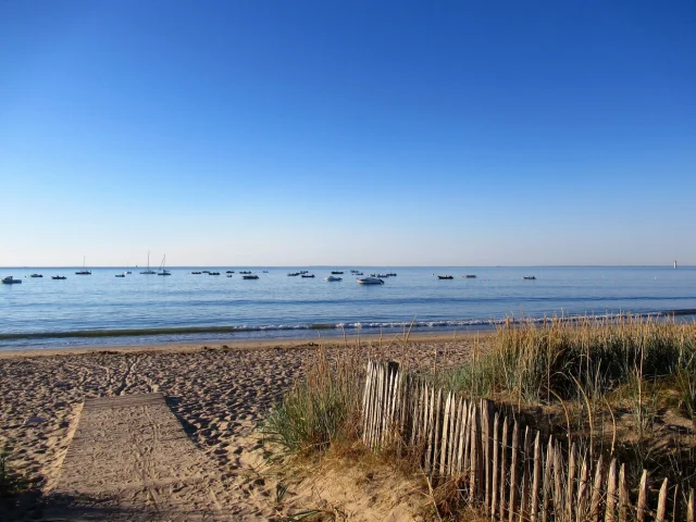 Plage tranquille à Rivedoux avec des bateaux flottant au loin.