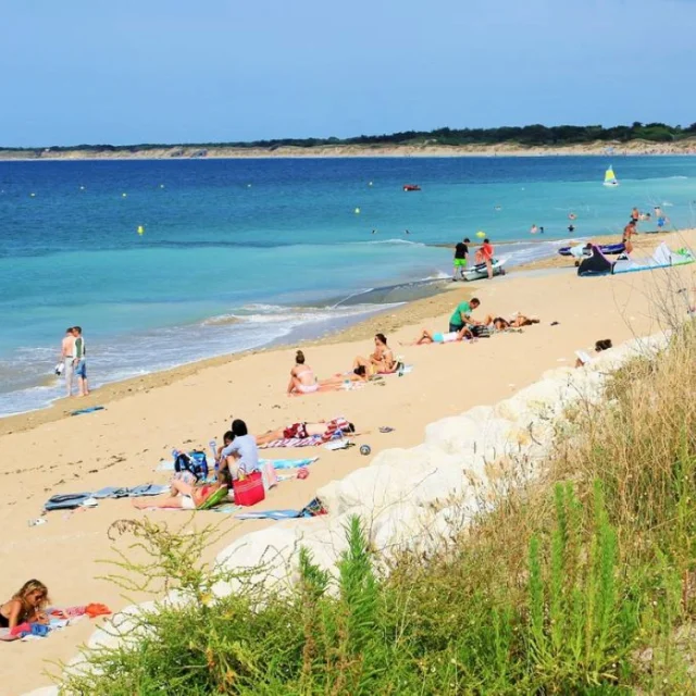 Plage de sable avec des personnes profitant du soleil et de l'eau.