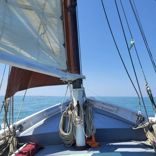 Vue de la proue d'un voilier naviguant sur une mer calme.