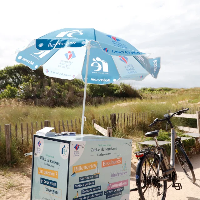 Remorque vélo d'accueil mobile équipée d'un parasol, stationnée dans la nature.