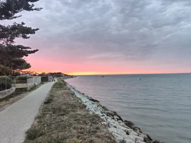 Sentier du littoral au bord de l'eau, éclairé par un coucher de soleil rose