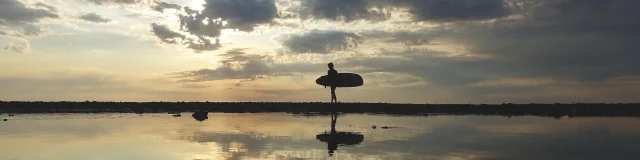 Surfeur marchant sur la plage au coucher de soleil