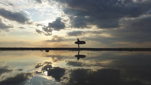 Surfeur marchant sur la plage au coucher de soleil