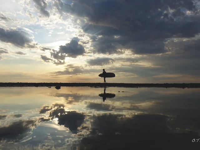 Surfeur marchant sur la plage au coucher de soleil