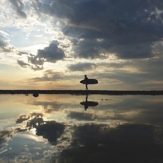 Surfeur marchant sur la plage au coucher de soleil