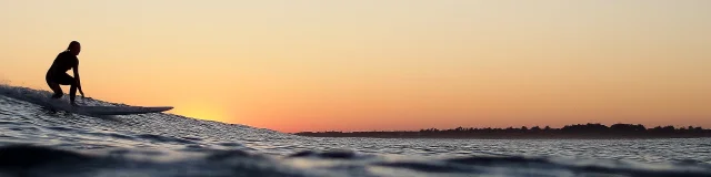 Un surfeur attrapant une vague au coucher de soleil sur l'île de Ré