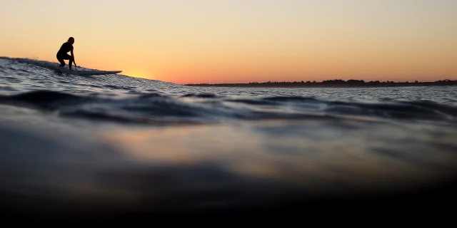 Un surfeur attrapant une vague au coucher de soleil sur l'île de Ré