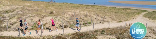 Groupe de personnes courant sur un chemin de sable près de la plage sous un ciel bleu.