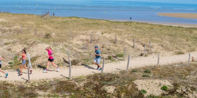 Groupe de personnes courant sur un chemin de sable près de la plage sous un ciel bleu.