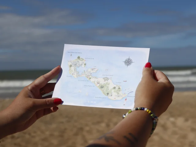 Personne tenant une carte postale de l'île de Ré avec la mer en arrière-plan.