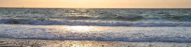 Coucher de soleil sur une plage de galets avec des vagues douces et un ciel doré.